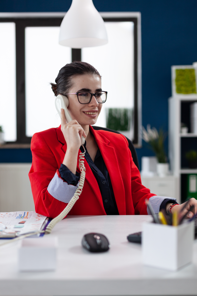 smiling-entrepreneur-with-glasses-phonecall-sitting-startup-desk-businesswoman-red-jacket-listening-employee-phone-small-business-owner-casual-conversation